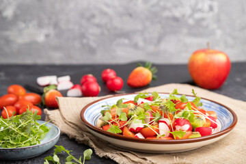 Vegetarian fruits and vegetables salad of strawberry, kiwi, tomatoes, microgreen sprouts on black and gray background. Side view, selective focus, copy space.