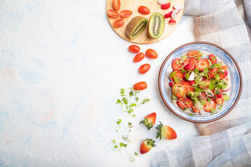 Vegetarian fruits and vegetables salad of strawberry, kiwi, tomatoes, microgreen sprouts on white concrete background. Top view, copy space.