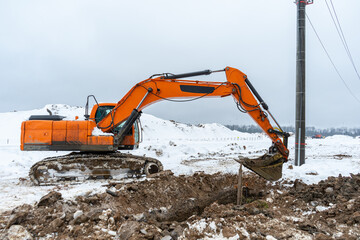 Fototapeta na wymiar A large orange excavator digs the ground to repair and lay underground utilities and cables for electricity and communications