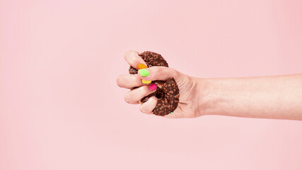 Female hand squeezing chocolate donut on pink background