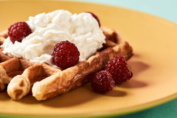 Close up shot of a traditional Belgian waffle with cream cheese and fresh raspberries on yellow plate