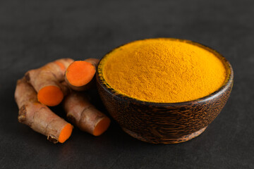 Turmeric powder in a black wooden bowl and fresh turmeric (curcumin) on black background,spices.
