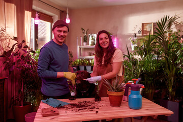 Happy young caucasian couple transplanting plants at home