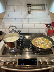 New York. 2021. Chinese meal being cooked using a wok. Noodles and chickem, mushrooms, scallions, carrot cooking on a modern gas oven.