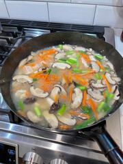 New York. 2021. Chinese meal being cooked using a wok. Chinese meal of chicken, sliced carrots, sliced scallions, ginger,and mushrooms cooking in a wok.