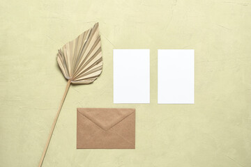 Two white blank business cards mockup, dried palm leaf and craft envelope on a beige stucco grunge background. Stationery still life. Top view, flat lay.