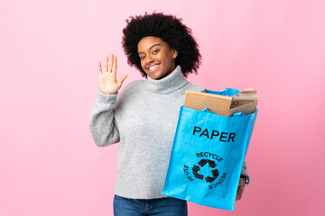 Young African American woman holding a recycle bag isolated on colorful background saluting with hand with happy expression