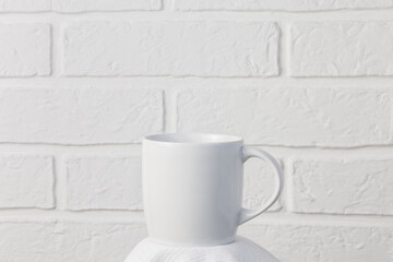 Household utensils, a white cup stands on a napkin against the background of a kitchen stone brick wall of a milky shade, the concept of clean dishes