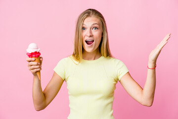 Young russian woman eating an ice cream isolated receiving a pleasant surprise, excited and raising hands.