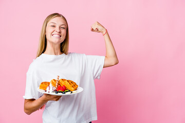 Young russian woman eating a waffle isolated raising fist after a victory, winner concept.