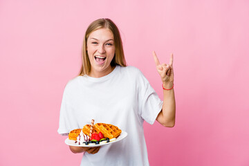 Young russian woman eating a waffle isolated showing a horns gesture as a revolution concept.