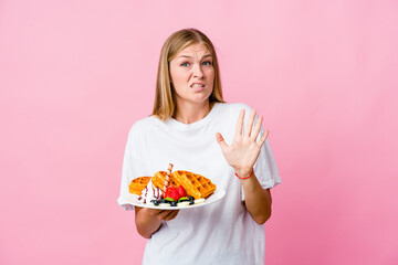 Young russian woman eating a waffle isolated rejecting someone showing a gesture of disgust.