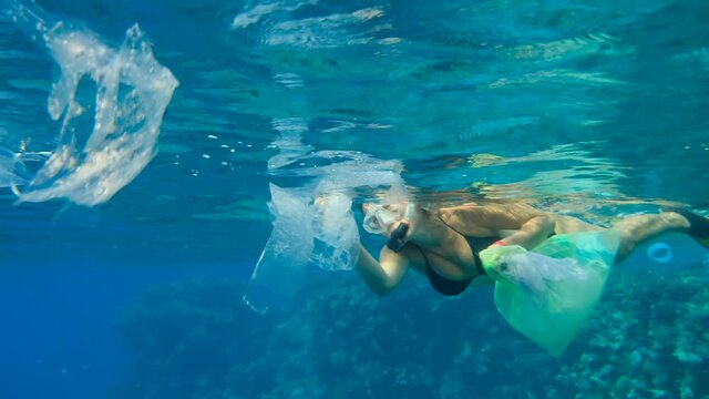 Woman in mask and fins swims and collects plastic debris under surface of blue water. Snorkeler cleaning Ocean from plastic pollution. Female snorkeler catches plastic trash from the water