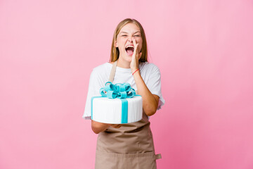 Young russian baker woman holding a delicious cake shouting excited to front.