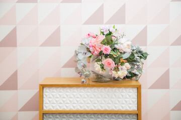 A vase of flowers on a chest of drawers near the wall with a geometric pattern