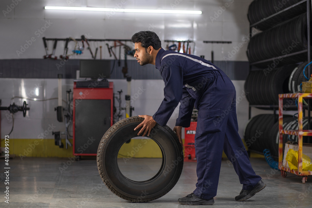 Wall mural Mechanic carrying a tyre at motor garage	