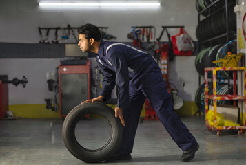 Mechanic carrying a tyre at a tyre service and repair center	