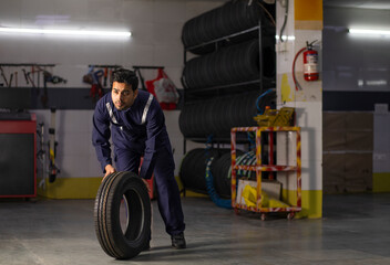 Full-length Mechanic carrying a tyre at motor garage	