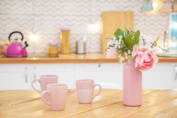 Fototapeta na wymiar Pink vase with flowers and mugs for tea on the table in a light kitchen