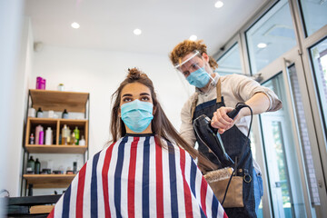 Fototapeta na wymiar Woman wearing face mask getting fresh styling at a hairdresser shop. Adult woman at hairdresser wearing protective mask due to coronavirus pandemic. A hairdresser with security measures for Covid-19