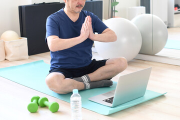 自宅でノートパソコンでオンラインヨガをする白髪のシニア男性