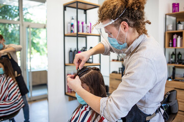 Hairdresser with security measures for Covid-19, cutting hair of woman with medical mask at beauty salon, free space. A hairdresser with security measures for Covid-19