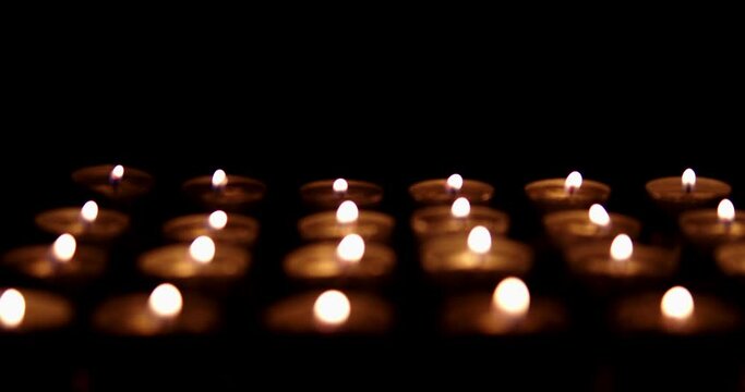 Many small candles on a black background. Smooth sliding of candles. The focus changes smoothly. Candles flicker in the dark. Beautiful view of shimmering flickering twinkling lights.