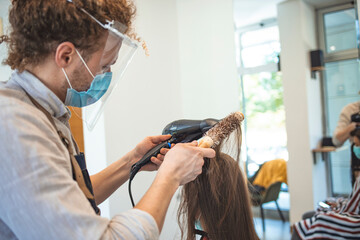Happy woman with protective face mask feeling satisfied after getting her hair styled at...