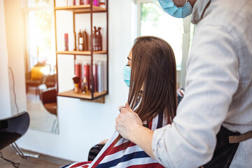 Hairdresser with mask enjoying to work again in her hair salon after lockdown is over. Woman have hair cutting at hair stylist during pandemic isolation, they both wear protective equipment.