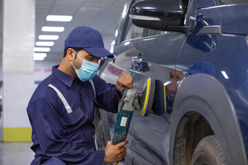 mechanic polishing a car with an electric orbital polisher in auto repair Shop	