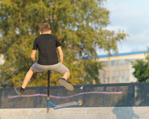 Teenager performs a trick in the city skate  park. Push scooter. He jumping over an obstacles. Extreme sports is very popular among youth. Back, rear view