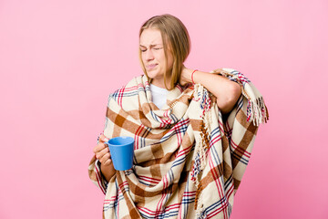 Young russian woman wrapped in a blanket drinking coffee suffering neck pain due to sedentary lifestyle.