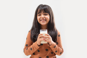 A HAPPY YOUNG GIRL LOOKING AT CAMERA WHILE HOLDING A GLASS OF MILK	