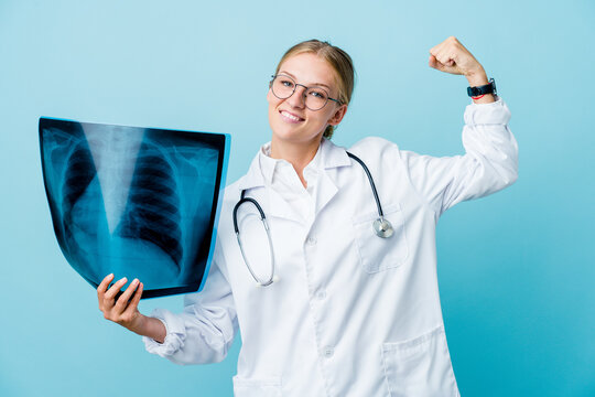 Young Russian Doctor Woman Holding A Bone Scan On Blue Showing Strength Gesture With Arms, Symbol Of Feminine Power