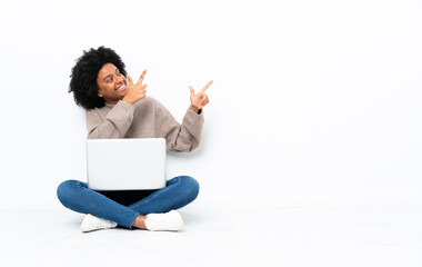 Young African American woman with a laptop sitting on the floor pointing with the index finger a great idea