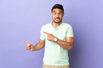 Young handsome man isolated on purple background frightened and pointing to the side