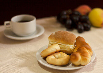 Breads or buns in white plate decorated with a cup of coffee and fruits on background