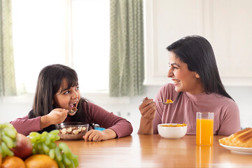 A YOUNG DAUGHTER LOOKING AT MOTHER WHILE HAPPILY EATING BREAKFAST	