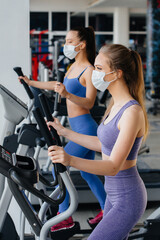 Fototapeta na wymiar Two young beautiful girls exercise in the gym wearing masks during the pandemic. Social distancing in public places.