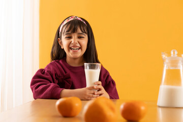 A GIRL CHILD HAPPILY LAUGHING WHILE HOLDING A GLASS OF MILK	