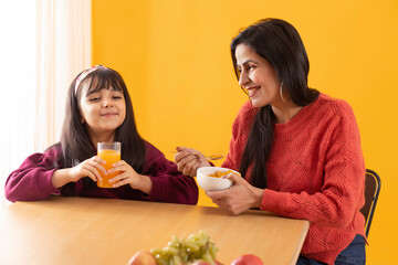 A DAUGHTER AND MOTHER HAPPILY SITTING TOGETHER WHILE DRINKING JUICE AND EATING CORNFLAKES	