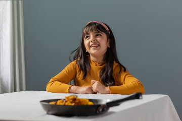 A YOUNG GIRL HAPPILY LOOKING ABOVE AND THINKING WHILE FOOD IS KEPT ON TABLE	