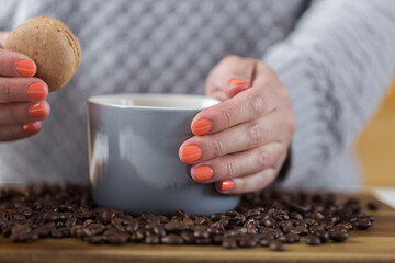 Female hand holding a mug of coffee and a macaroon.