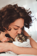 Woman kissing her lovely cat at the bed at morning