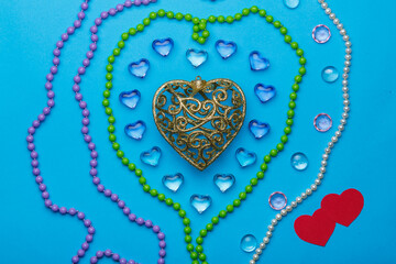 On a blue background, there is a heart of transparent pebbles in the shape of hearts in the middle of a bunch of jewelry next to it.