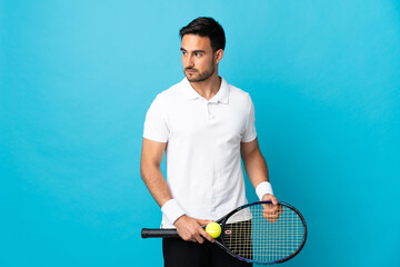 Young handsome man isolated on blue background playing tennis