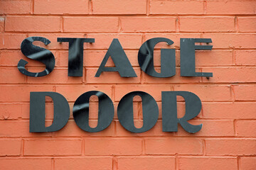 Isolated Stage Door sign in black text on bright orange brick wall