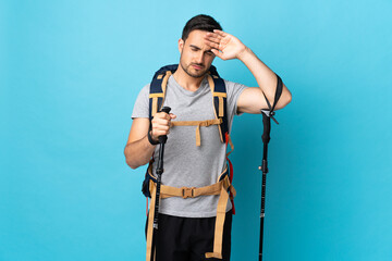 Young caucasian man with backpack and trekking poles isolated on blue background with tired and sick expression