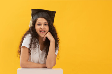 A HAPPY TEENAGER SITTING AND SMILING AT CAMERA WHILE WEARING GRADUATION CAP	