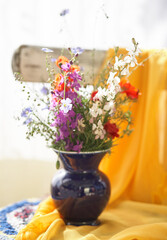 Still life with fresh wild flowers in vase on vintage chair